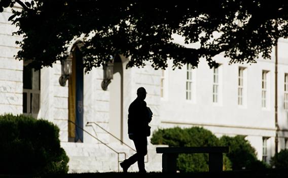 Silhouette of a man walking under trees on campus.