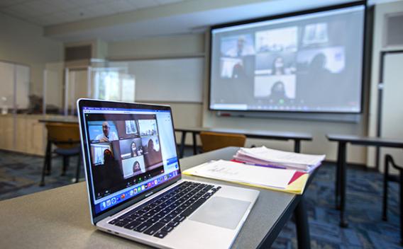 Open laptop with online meeting projected onto screen.