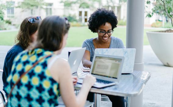 Three woman with laptops sitting at a table outside.